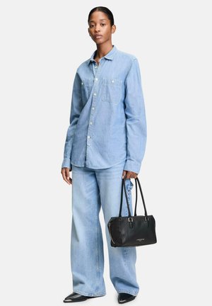Hellblaues Denimhemd mit langen Ärmeln und zwei Brusttaschen, kombiniert mit weit geschnittenen hellblauen Jeans. Schwarze Lederhandtasche mit Schulterriemen.