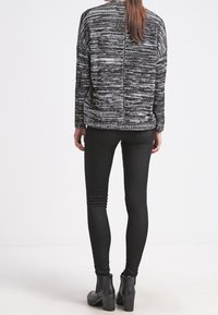 Kvinna som står vänd bort, iklädd en svart och vit mönstrad tröja, svarta skinny jeans och svarta klackiga ankelstövlar.