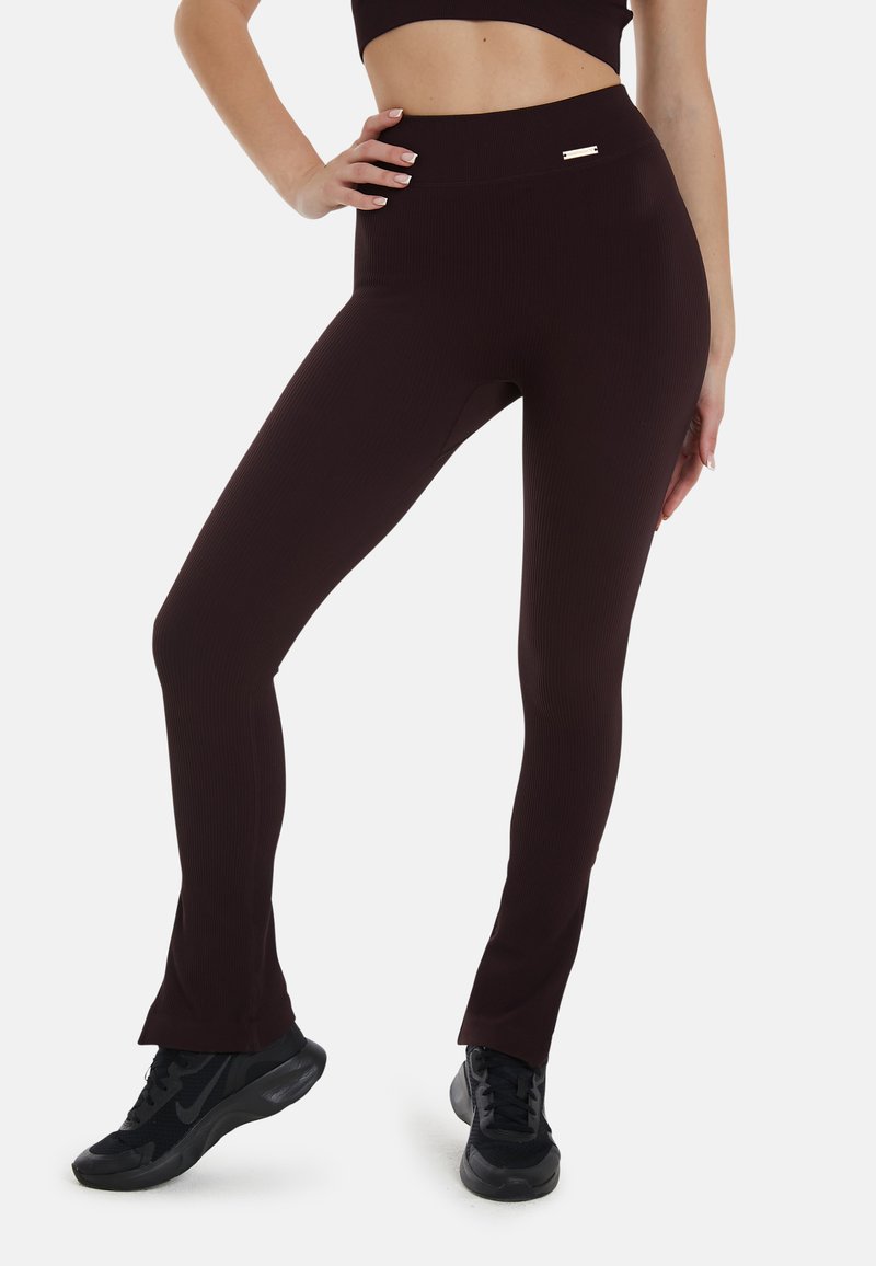 Bordeaux ribbel leggings met een hoge taille, flared zoom en een kleine gouden accent op de tailleband. Gede gedragen met zwarte sportschoenen.