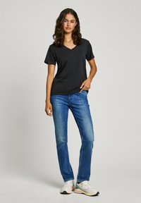 T-shirt noir à manches courtes en V associé à un jean droit bleu et des chaussures de sport blanches. Design simple, tissu lisse, sans motifs visibles.