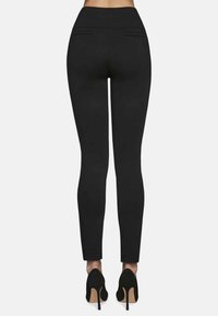 Czarne legginsy z wysokim stanem, z dwoma tylnymi kieszeniami i dopasowanym zwężającym się krojem nogawki, w połączeniu z czarnymi szpilkami.