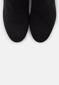 Bottines en cuir suede noir avec une texture lisse, un design à bout pointu et sans matériel ni accents visibles. Vue de dessus.