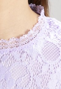 Levandulový krajkový top s propracovanými květinovými vzory a vykrojeným, vyšívaným výstřihem. Jemná textura s lehkým pocitem.