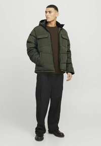 Padded olivgrüne Jacke mit Kapuze, mit Fronttaschen und Reißverschluss, kombiniert mit dunklen Cargo-Hosen und schwarzen Schuhen.