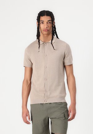Lühikeste varrukatega beež kootud polo särk tekstuurse mustriga, klassikalise krae ja nööpide ettepanekuga. Koos roheline kargoshorts.