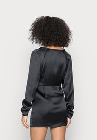 Musta satiini mekko pitkillä hihoilla, istuvalla vyötäröllä ja lyhyellä pituudella. Sileä rakenne ja minimalistinen muotoilu, jossa on pyöreä kaula-aukko.