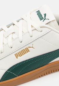 Vita läder sneakers med gröna detaljer, guld-logotyp och en texturerad gummisula. Har snörningsdesign och vadderad plös.