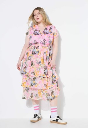 Robe florale avec une base rose, design superposé, manches courtes et ceinture à nouer. Associée à des chaussettes blanches avec des rayures roses et des baskets noires.