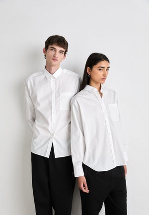 Hvite skjorter med knapper foran, lette materialer, klassisk krage, kombinert med svarte bukser, som viser et minimalistisk design.