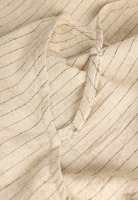Tissu beige à fines rayures verticales noires avec un petit anneau en boucle et un détail en métal sur une surface légèrement froissée.