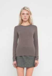 Top cu mâneci lungi și guler rotund dintr-un material moale maro. Asortat cu o fustă gri texturată, evidențiind o siluetă conică și un design minimalist.