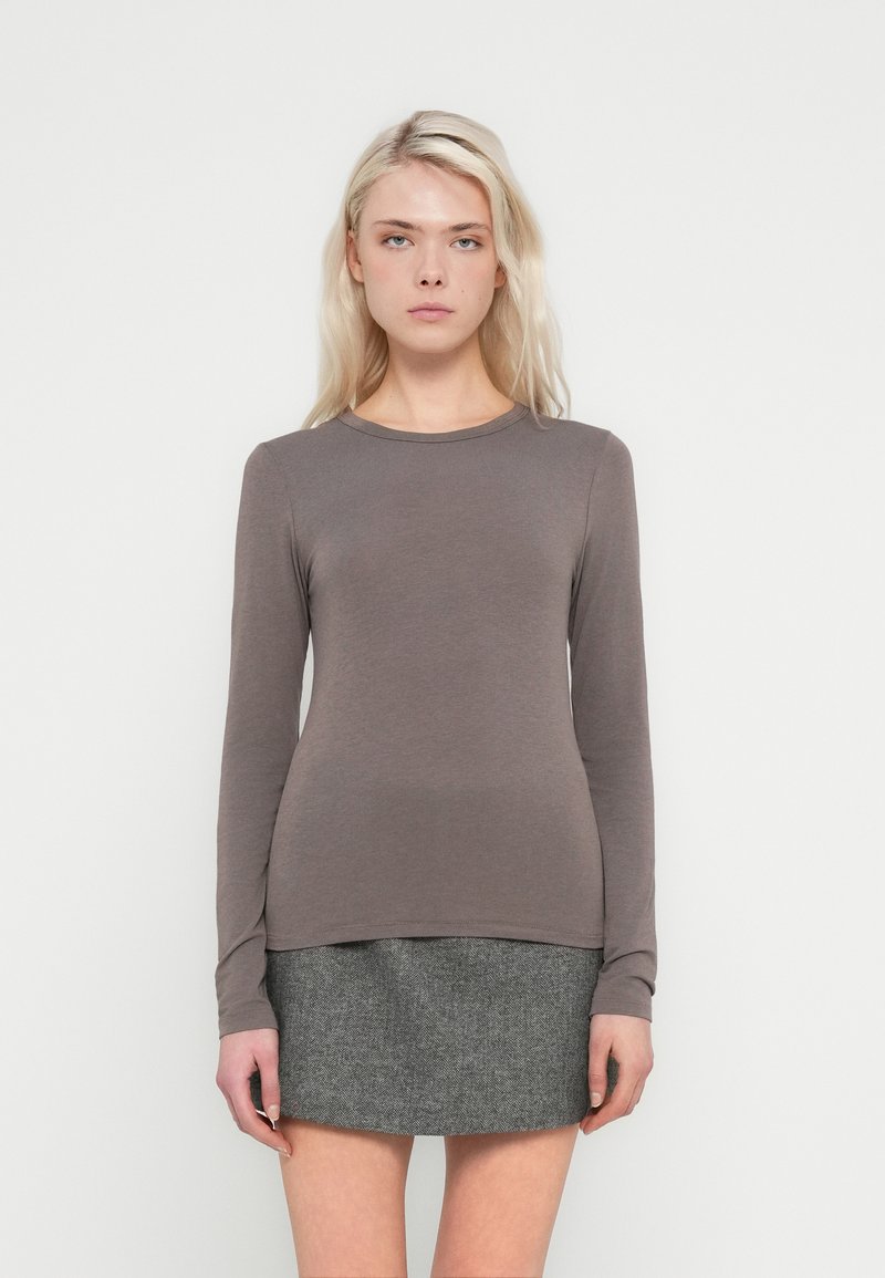 Top cu mâneci lungi și guler rotund dintr-un material moale maro. Asortat cu o fustă gri texturată, evidențiind o siluetă conică și un design minimalist.