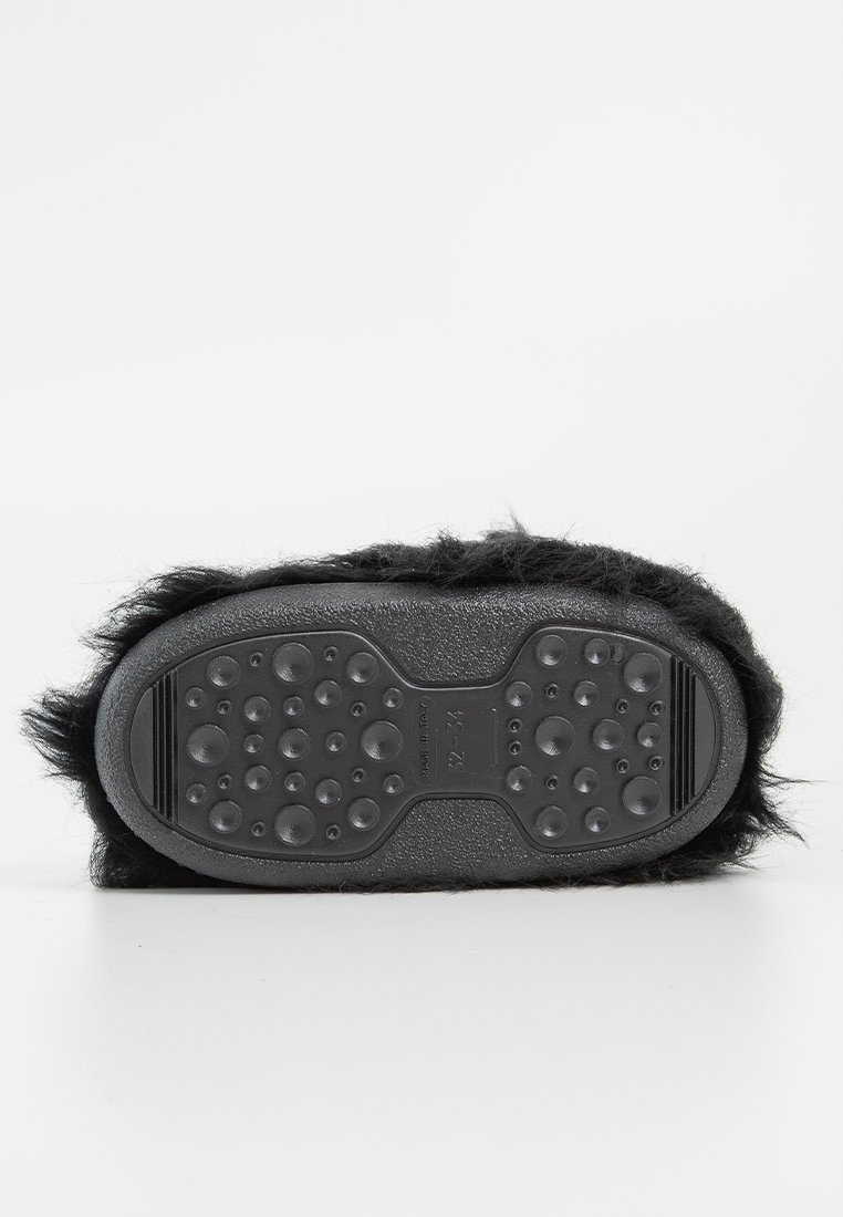 Zwarte fuzzy slipper met een zool van textuur rubber, voorzien van ronde grip-structuren voor traction en een zachte, pluche bovenrand.