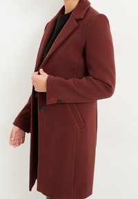 Viininpunainen villakangastakki, jossa räätälöity muotoilu, lovettu kaulus, yksirivinen nappikiinnitys, sivutaskut ja sileä pinta.