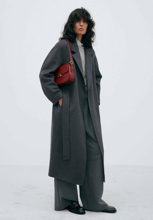 Gray wool overcoat with wide sleeves, paired with gray tailored trousers. Red leather shoulder bag and black loafers complete the look.