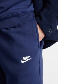 Marinblå Nike sweatpants i mjukt material, med en vit logotyp på låret och en sidficka, avslappnad passform och elastisk midja.