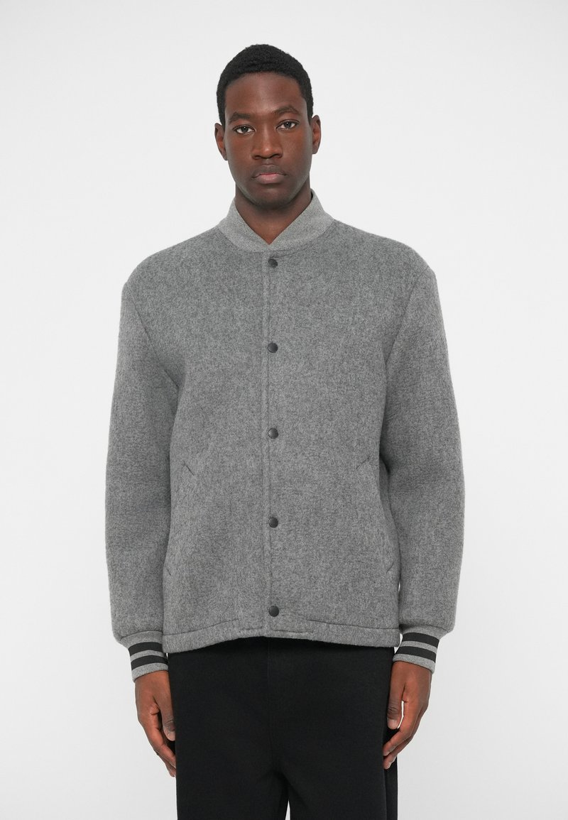 Γκρι μάλλινο σακάκι με ψηλό γιακά, εμπρός κουμπιά και ραμμένη μανσέτα με μαύρες και λευκές ρίγες. Υφή υφάσματος, δομημένη εφαρμογή.