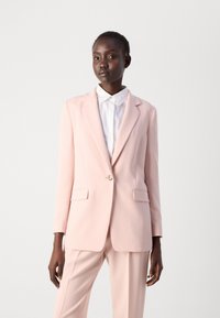 Helles rosa Sakko aus glattem Stoff, mit einer einzelnen Knopfverschluss, Reverskragen und zwei Vorderseiten-Taschen. Gestylt über einem weißen Hemd.
