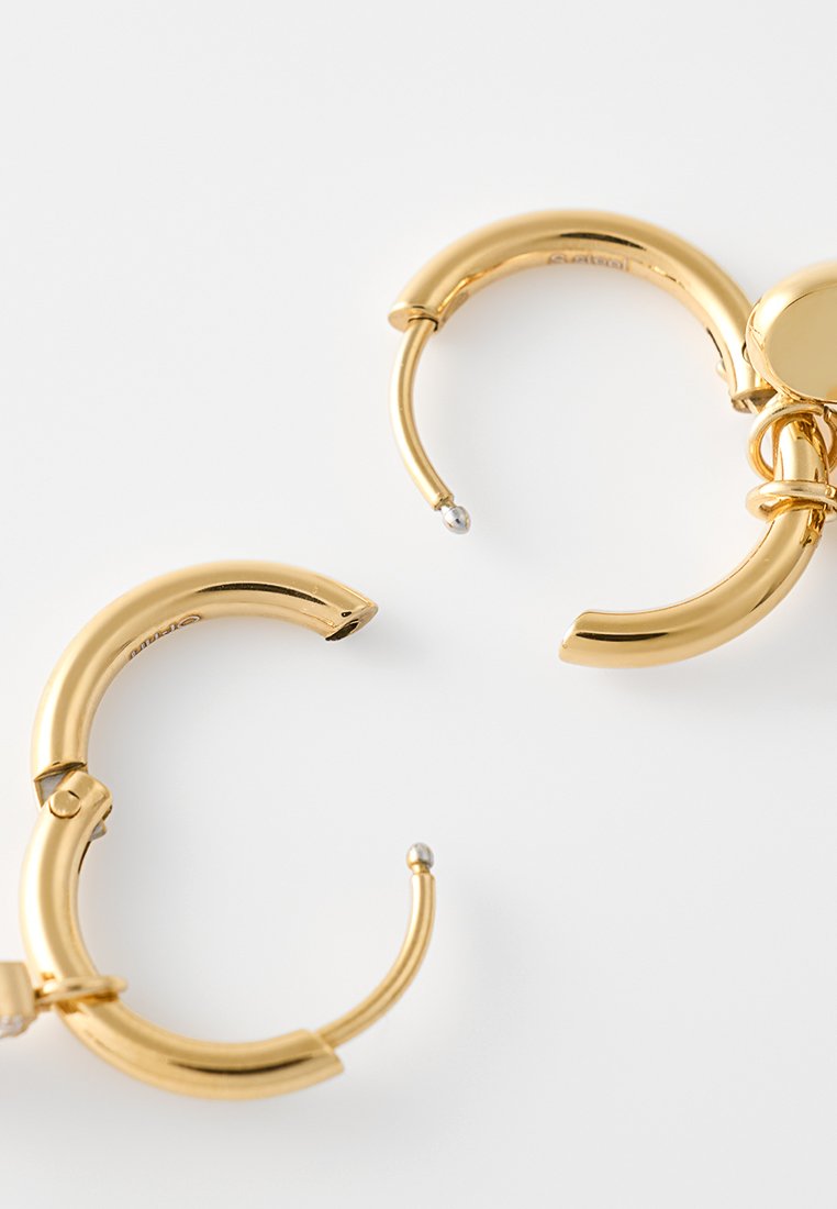Para otwartych, wypolerowanych złotych kolczyków w kształcie obręczy z zapięciem na zawiasy na białym tle.