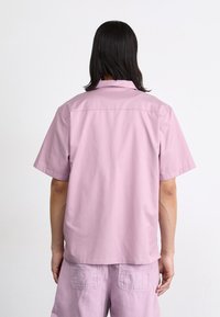 Korte mouwen, lichtroze shirt met een relaxte pasvorm, zachte textuur en een standaard kraag. Bevat een yoke-detail aan de achterkant.