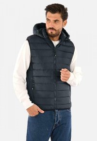 Gilet imbottito blu navy con cappuccio, zip frontale e tasche laterali, caratterizzato da un'imbottitura trapuntata orizzontale e una texture liscia. Indossato su una camicia bianca.