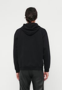 Haut à capuche noir en tissu doux et texturé, doté d'une grande capuche et de poignets côtelés. Design simple et coupe décontractée avec un dos uni.