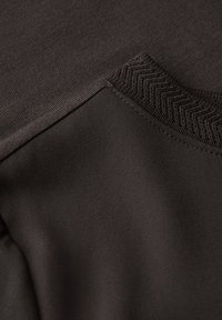 Dunkelbrauner sportlicher Stoff mit glatter Oberfläche, strukturiertem Ripp-Halsausschnitt und kontrastierenden Nähdetails.