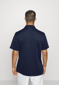 Marineblaues Kurzarm-Polo-Shirt mit klassischem Kragen, glatter Textur und dezentem Stichdetail, von hinten gezeigt.