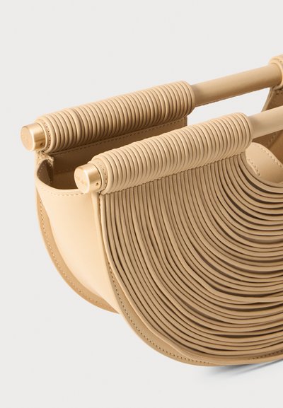Geantă din piele bej cu un design curbat și pliat, având mânere ribbed și o textură netedă. Stil minimalist cu detalii notabile.