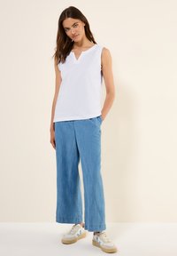 Top blanco sin mangas con escote en V, combinado con pantalones de pierna ancha de color azul claro; la modelo lleva zapatillas blancas con detalles azules.
