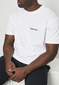 White cotton t-shirt with short sleeves, featuring a small black embroidered logo "forgotten faces" on the left chest area.