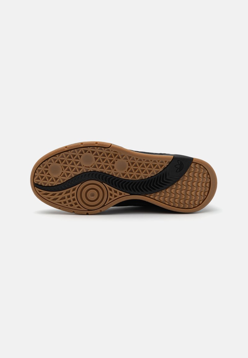 Suela de zapatilla negra con un fondo de goma texturizada, que presenta un patrón negro ondulado y puntos de tracción circulares para un mejor agarre.