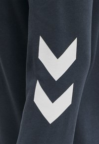 Marinblå sweatshirt ärm med två vita chevronränder, tillverkad av mjuk bomull med en slät textur. Enkel och modern design.
