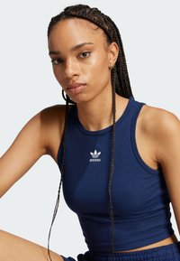 Mornarsko modra rebrasta majica brez rokavov z oprijetim krojem, ki ima majhen bel Adidasov logotip na prsih in tanke naramnice. Ramena so vidna.