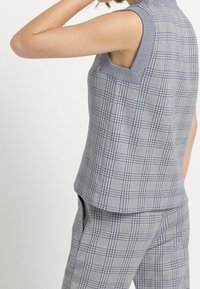 Šedý a modrý kostkovaný top bez rukávů s náprsními kapsami a kulatým výstřihem, vyrobený z texturované látky s pevným střihem.