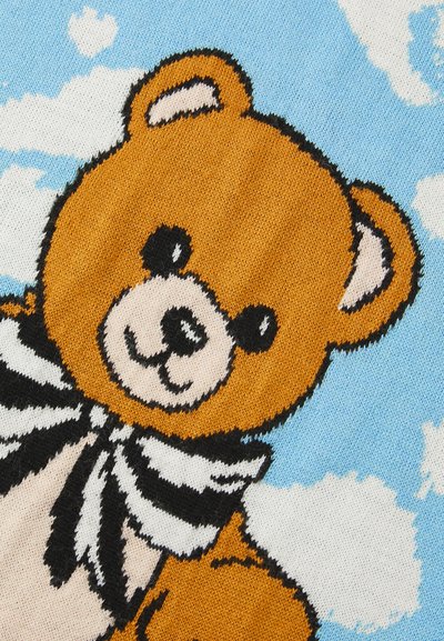 Rudas meškos personažas su baltu šaliku, priešais mėlyno dangaus foną su debesimis. Minkšta megzta tekstūra ir animacinis stiliaus dizainas.