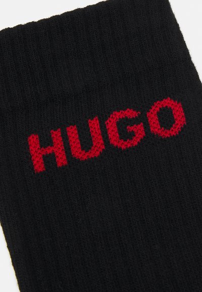 Chaussettes noires en maille avec une texture côtelée, ornées d'un logo tricoté rouge "HUGO" affiché en évidence sur la partie supérieure.