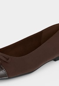 Καφέ γυναικείο flat παπούτσι με λεπτομέρεια φιόγκου και υφασμένη σκουρόχρωμη καφέ μύτη, χαμηλή μαύρη σόλα και λεία ματ φινίρισμα.