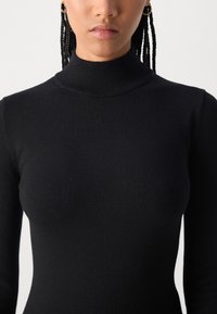 Black turtleneck sweater made of soft knit fabric, featuring a fitted silhouette and long sleeves, with a smooth texture and no additional patterns.