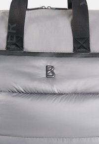 Gray puffer-style bag with smooth, shiny texture. Features black webbed straps with text and a raised 'B' logo on the front. Zipper closure.