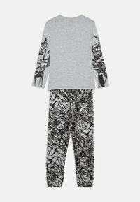 Graues Langarmshirt mit schwarzem grafischen Design an den Ärmeln, kombiniert mit schwarzen gemusterten Hosen, die verschiedene Cartoon-Grafiken zeigen.