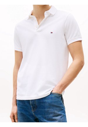White polo shirt made of cotton, featuring a collar, three-button placket, and a small logo on the chest. Paired with blue jeans.