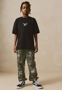 Black oversized t-shirt with white "New York 92" text, paired with green camouflage cargo pants and black sneakers with white accents.
