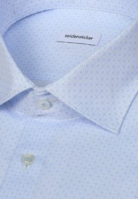 Chemise habillée bleu clair à motifs avec des boutons blancs et l'étiquette de marque "seidensticker" à l'intérieur du col.