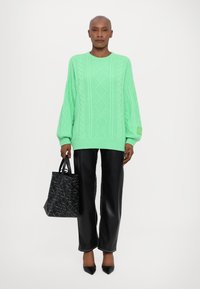 Maglione verde menta a coste con maniche oversize, abbinato a pantaloni larghi in ecopelle nera e una borsa a tracolla nera con texture.