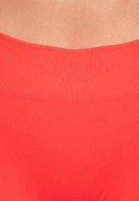 Koraalkleurige sportieve tailleband met een geribbelde structuur, ontworpen voor comfort. Gladde stof eronder, die een naadloze uitstraling benadrukt.