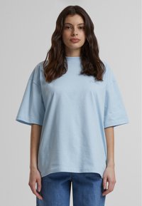 Camiseta de gran tamaño azul claro confeccionada en suave algodón. Presenta mangas cortas y un escote redondeado, con un sutil logo bordado en el pecho.