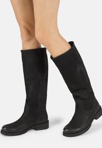 Bottes noires en cuir montant jusqu'au genou, avec une surface lisse, un bout rond et un petit talon empilé ; elles présentent un design de tige légèrement flasque.