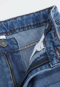 Niebieskie dżinsy o kroju z zamkiem błyskawicznym i zapięciem na guzik, z widocznymi detalami ściegów i teksturowanym wykończeniem materiału wewnątrz pasa.