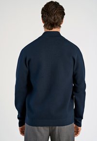 Sininen neulepusero, jossa on mock-kaulus, pitkät hihat ja tasainen pinta. Ominaisuuksiin kuuluu suora helma ja ribbauskärjet.